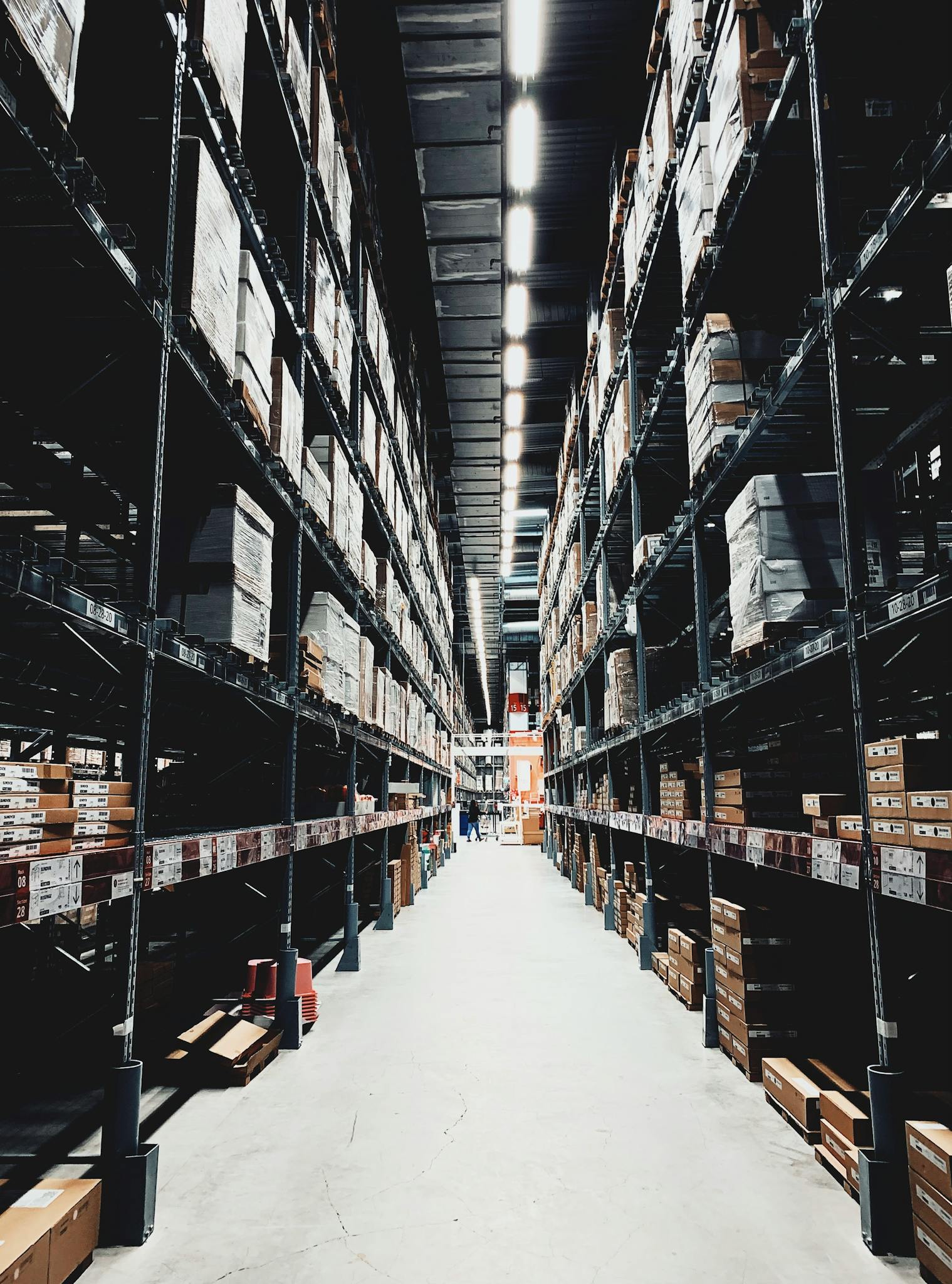 A wide aisle in a large warehouse filled with stacked boxes on high shelves.